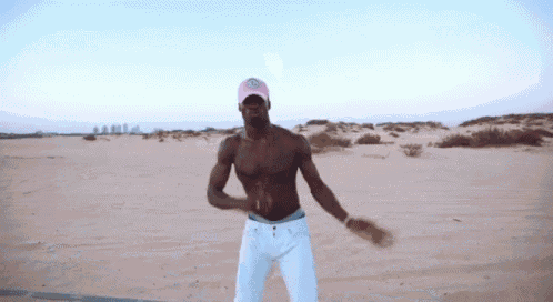 a shirtless man in a pink hat and white pants is dancing in the desert