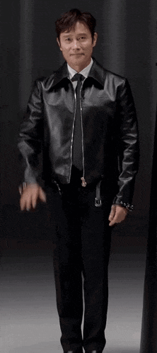 a man in a leather jacket and tie is waving his hand .