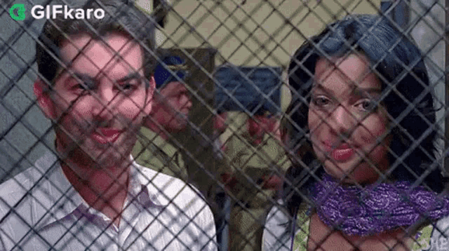a man and a woman are standing next to each other behind a fence .