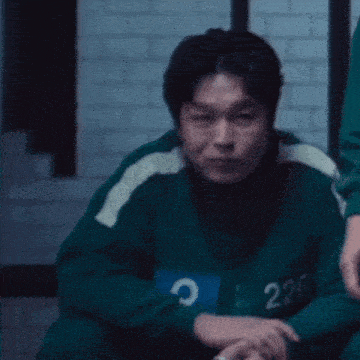 a man in a green sweater with the number 226 on it is sitting on the floor in a dark room .
