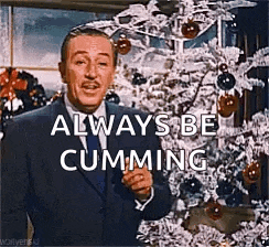a man in a suit and tie is standing in front of a christmas tree and saying `` always be cumming '' .