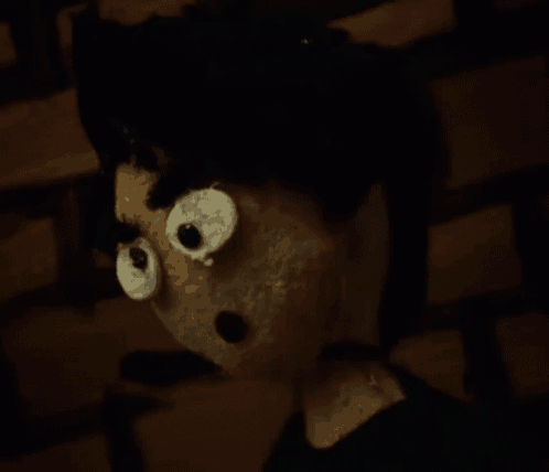 a stuffed animal with big eyes and black hair is standing in front of a brick wall