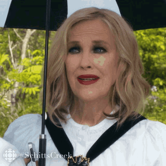 a woman holding a black umbrella with the word schitts creek on the bottom right
