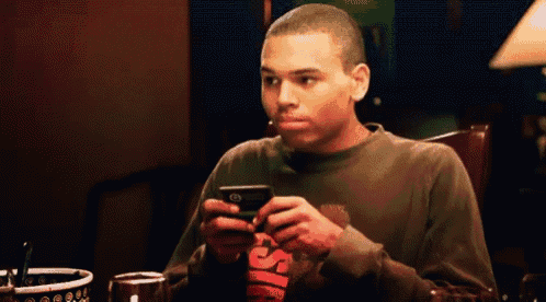 a man sitting at a table looking at a cell phone with the letter s on it