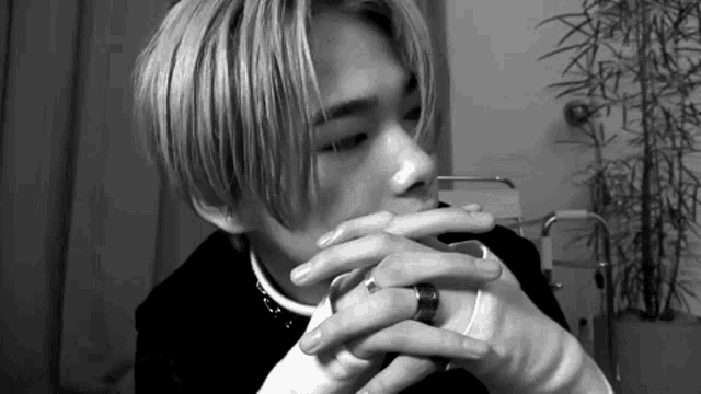 a black and white photo of a young man with a ring on his finger smoking a cigarette .
