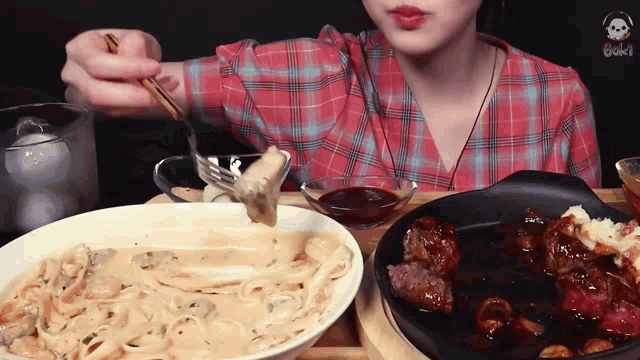 a woman in a plaid shirt is eating noodles and steak
