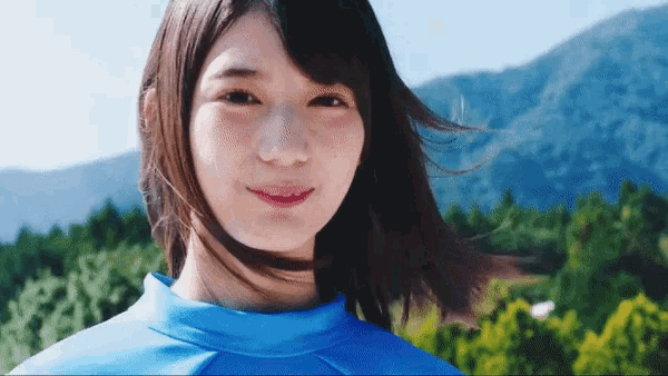 a woman in a blue shirt stands in front of a mountain range