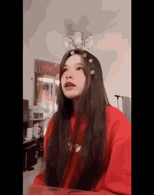 a girl with long hair is wearing a red sweater and has flowers in her hair .