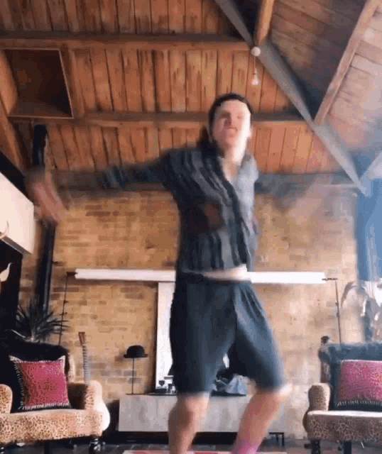 a man is dancing in a living room in front of a wooden ceiling