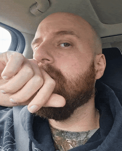 a bald man with a beard is covering his mouth with his hand