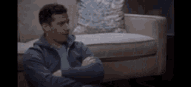 a man is sitting on a couch with his arms crossed .