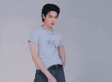a man wearing a white t-shirt and blue jeans is standing in front of a white wall .