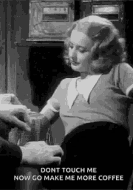 a woman is sitting in a chair talking to a man while a man touches her arm .