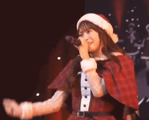 a woman in a santa hat and cape is singing into a microphone .
