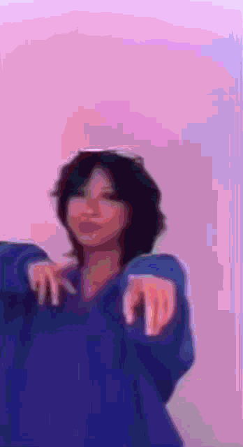 a woman in a blue sweater is pointing at the camera with her hands .