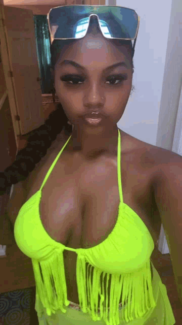 a woman in a neon yellow bikini and sunglasses takes a selfie .