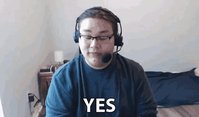 a man wearing headphones and glasses is sitting in front of a camera and saying yes .