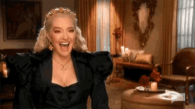 a woman is laughing in a living room wearing a black dress and a tiara .