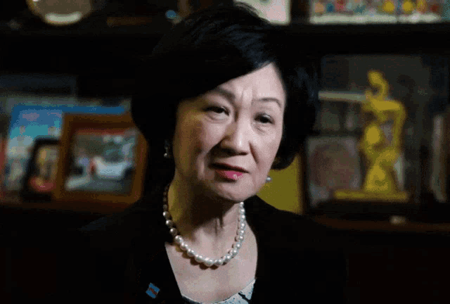 a woman wearing a pearl necklace and a ring is giving a thumbs up