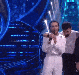 a man in a white suit is holding a microphone while standing on a stage