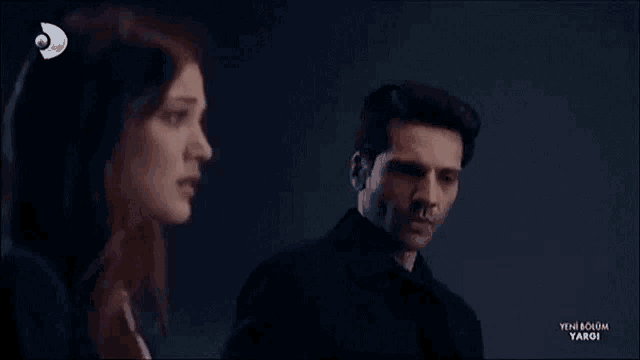 a man is holding a woman 's hand in a dark room while a tv show is playing .