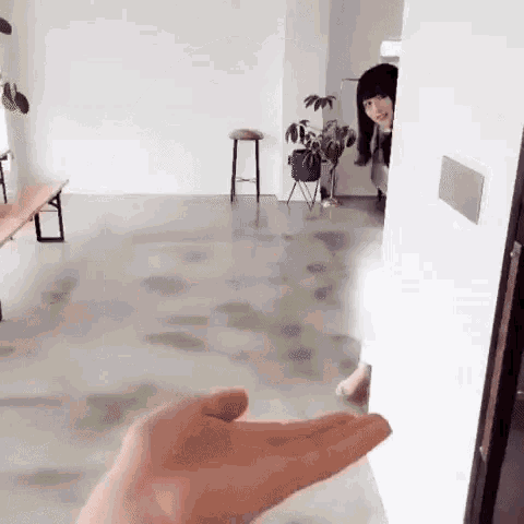 a person 's hand is reaching out towards a woman standing in a room .