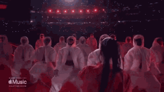a woman in a red dress is dancing with a group of people in white suits on a stage .