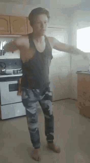a man in a black tank top and camo pants stands in a kitchen