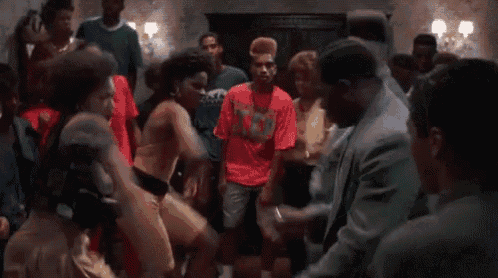 a group of people are dancing in a room while a man in a suit is standing in the middle of the room .