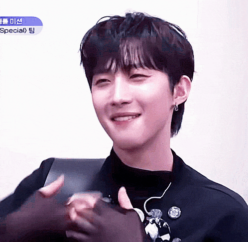 a young man in a black jacket is smiling and clapping his hands