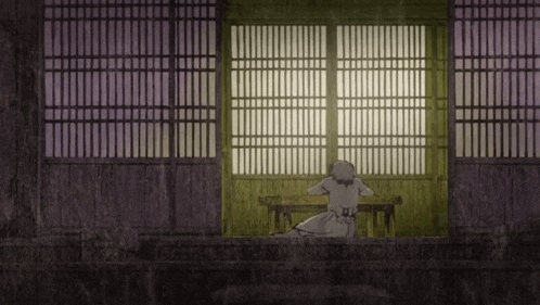a woman is sitting at a table in front of a window in a dark room .