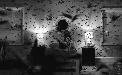 a black and white photo of a person laying on a bed with birds flying around them and the word uvel on the bottom right
