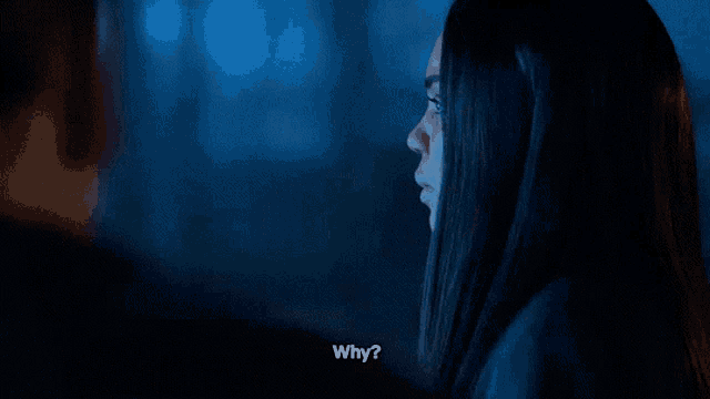 a woman is smiling and asking why while looking at a man in a dark room .