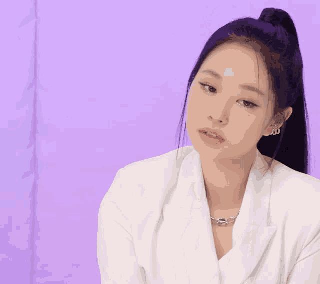 a woman wearing a white jacket and a necklace looks at the camera