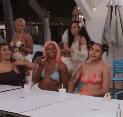 a group of women in bikinis are sitting at a table with drinks