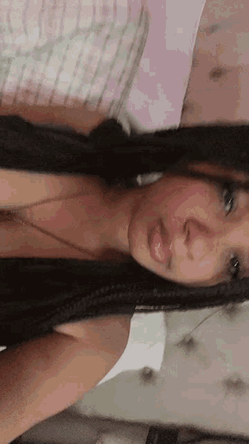 a woman with long black hair is laying on a bed with a necklace around her neck .
