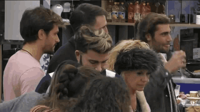 a group of people standing around a table in a kitchen .