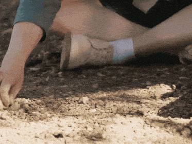 a person is kneeling on the ground and picking up rocks with their hand