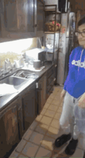 a person wearing a blue adidas sweatshirt stands in a kitchen