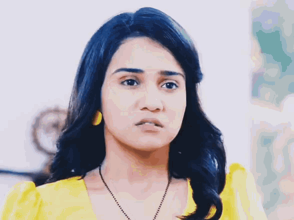 a woman wearing a yellow top and a black necklace has a sad look on her face
