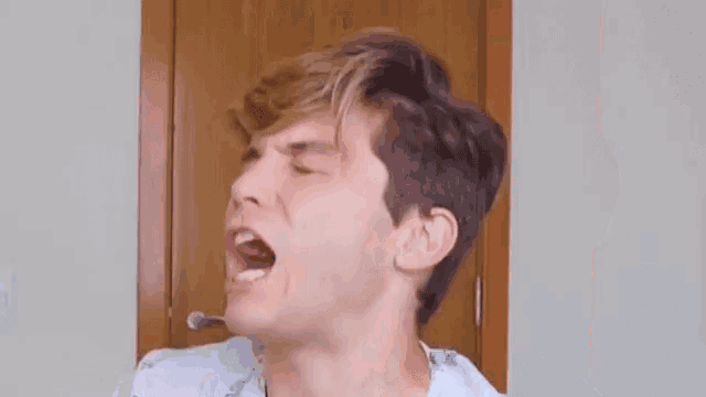 a young man is yawning with his mouth open while sitting in front of a door .
