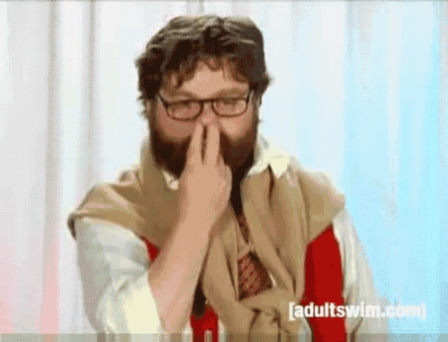 a man with a beard and glasses covering his nose with his hand .