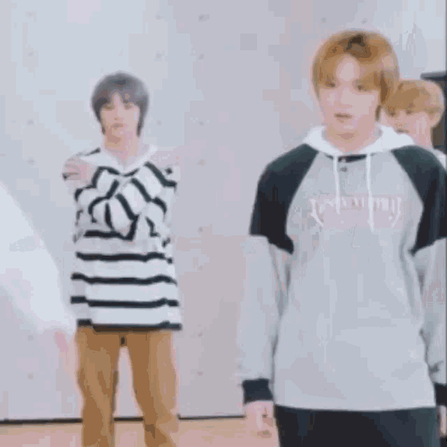 a group of young men are standing next to each other in a room . one of the men is wearing a striped shirt .