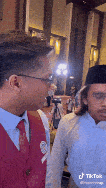 two men are standing next to each other and one has a tiktok sticker on his shirt