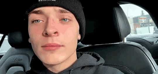 a young man wearing a black beanie and a black hoodie is sitting in a car