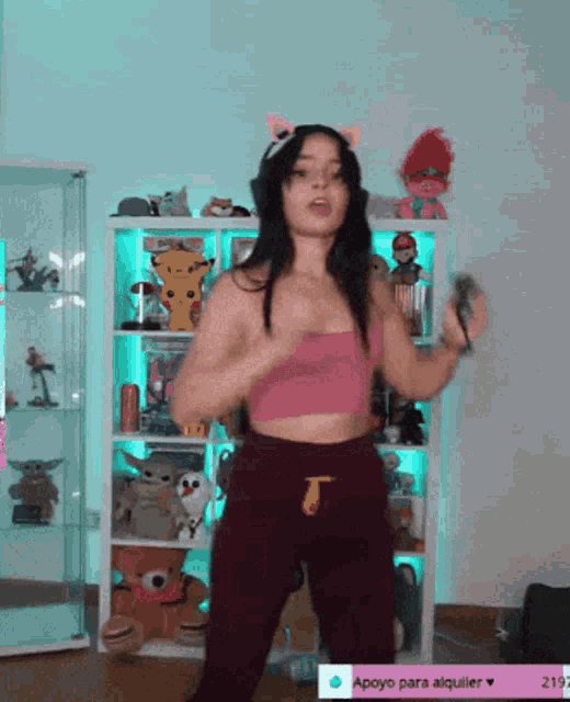 a woman in a pink top and purple pants is dancing in front of a shelf with stuffed animals