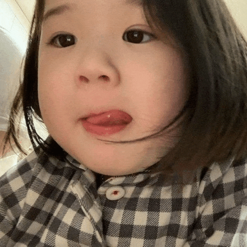a little girl wearing a plaid shirt is sticking out her tongue .