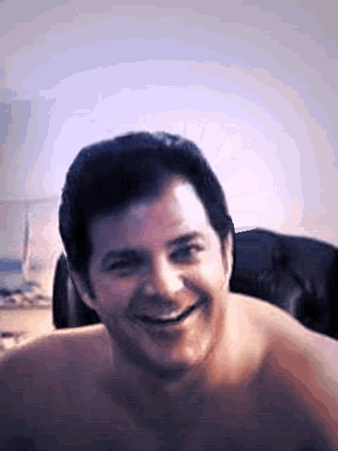 a shirtless man smiles for the camera in a blurry photo