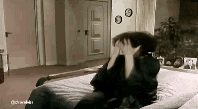 a man is sitting on a bed with his head in his hands .
