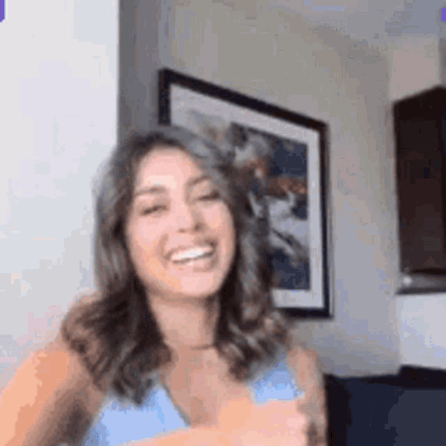 a woman in a blue tank top is smiling in front of a framed picture .